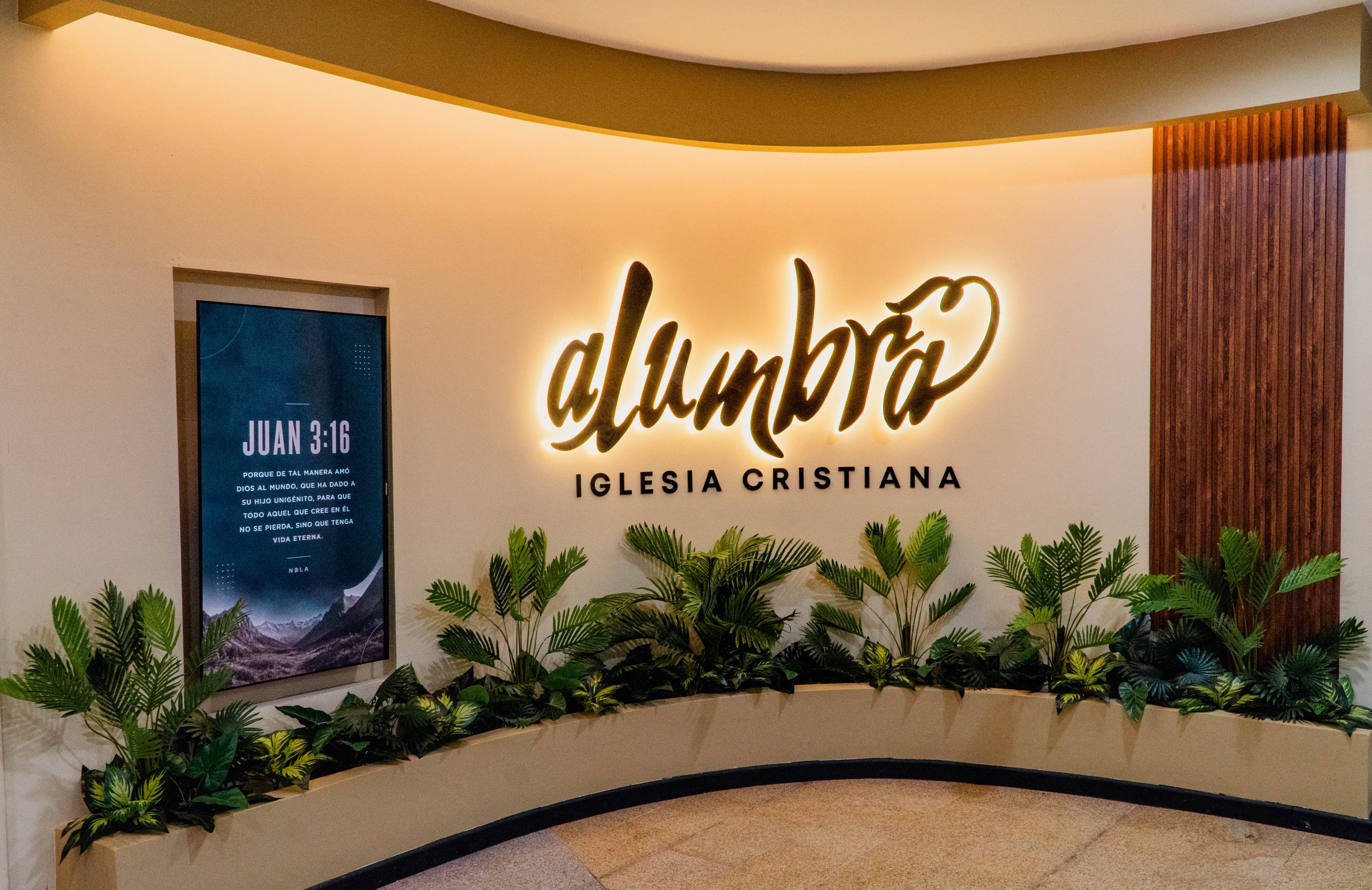 El muro del lobby con el letrero de Alumbra y el versículo de Juan 3:16